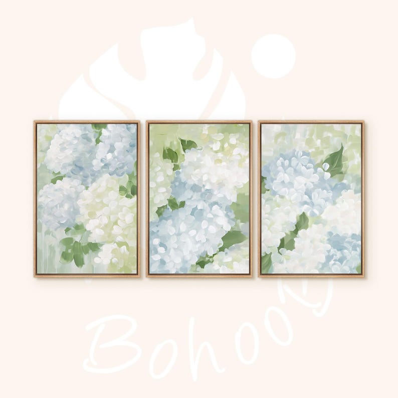 Puede incluir: Conjunto de tres l&aacute;minas art&iacute;sticas florales enmarcadas. Cada l&aacute;mina presenta una pintura de acuarela de flores de hortensia en tonos blancos, azules y verdes. La obra de arte se muestra en un marco de madera clara, creando un conjunto de arte mural coordinado.