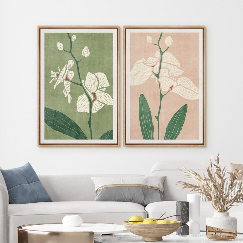 Pu&ograve; includere: Due stampe incorniciate di fiori di orchidea bianchi con foglie verdi su uno sfondo chiaro. La stampa a sinistra ha uno sfondo verde e la stampa a destra ha uno sfondo rosa chiaro.