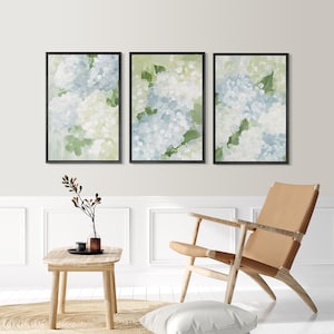 Puede incluir: Tres impresiones art&iacute;sticas florales enmarcadas. Cada impresi&oacute;n presenta una pintura de acuarela de flores de hortensia azules y blancas con hojas verdes sobre un fondo verde claro. Los marcos son negros y el arte se exhibe en un espacio de vida moderno.
