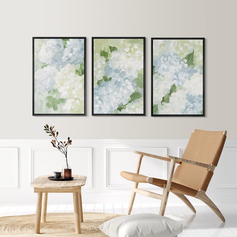 Puede incluir: Tres impresiones art&iacute;sticas florales enmarcadas. Cada impresi&oacute;n presenta una pintura de acuarela de flores de hortensia azules y blancas con hojas verdes sobre un fondo verde claro. Los marcos son negros y el arte se exhibe en un espacio de vida moderno.
