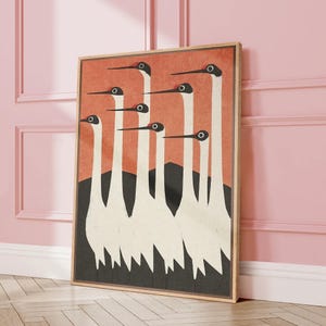 May include: Framed art print featuring a stylized illustration of seven white cranes with black and red details against a coral background. The birds stand in front of a black mountain range. The artwork is in a wooden frame.