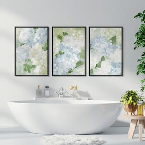 Puede incluir: Conjunto de tres l&aacute;minas art&iacute;sticas florales enmarcadas. Cada l&aacute;mina presenta una pintura al estilo acuarela de flores de hortensia en tonos azules, blancos y verdes. Los marcos negros se exhiben sobre una ba&ntilde;era blanca.