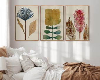 Può includere: Un set di tre stampe artistiche da parete incorniciate con illustrazioni botaniche. La stampa a sinistra mostra un fiore blu a ventaglio con foglie color cuoio. Quella centrale mostra un fiore giallo a blocchi con steli verdi. Quella a destra mostra un fiore rosa spinoso.