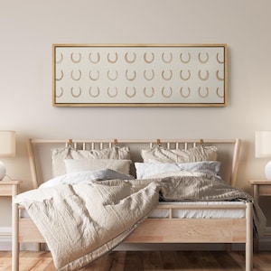 May include: A framed canvas art piece featuring a repeating pattern of tan horseshoes on a cream background. The artwork is displayed above a wooden bed frame with neutral-toned bedding, creating a cohesive and calming aesthetic. The room is decorated in a minimalist style.