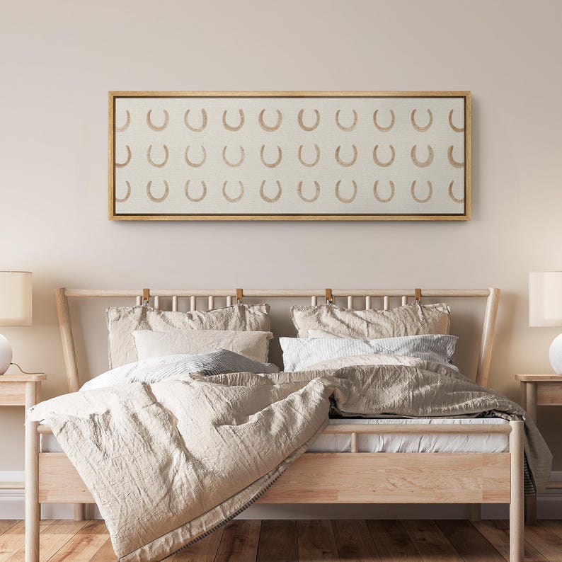 May include: A framed canvas art piece featuring a repeating pattern of tan horseshoes on a cream background. The artwork is displayed above a wooden bed frame with neutral-toned bedding, creating a cohesive and calming aesthetic. The room is decorated in a minimalist style.