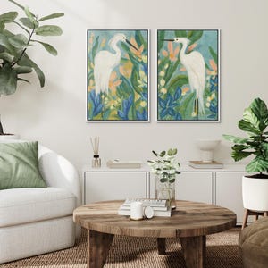 May include: Two framed art prints featuring white herons amidst colorful foliage. The artwork showcases a serene scene with blue, green, and peach tones. The heron's elegant form is central to the design, creating a calming aesthetic for home decor.
