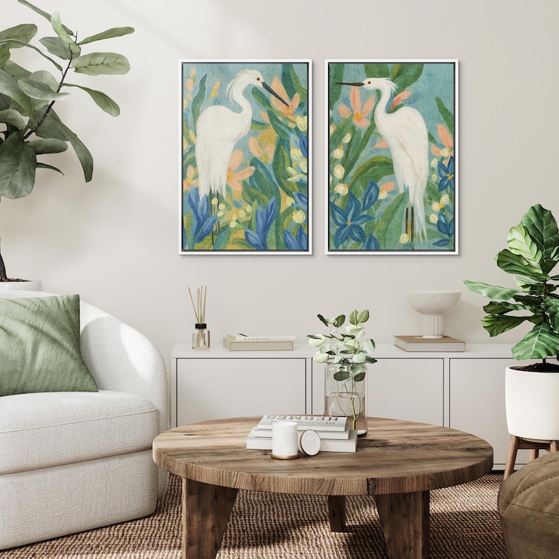 May include: Two framed art prints featuring white herons amidst colorful foliage. The artwork showcases a serene scene with blue, green, and peach tones. The heron's elegant form is central to the design, creating a calming aesthetic for home decor.