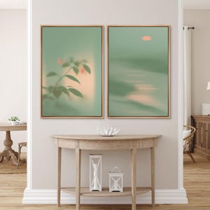 May include: Two framed abstract art prints. One features a blurred image of a plant with green leaves and peach-colored accents. The other depicts a sunset over water with a peach sun and green tones. Both are in wooden frames.
