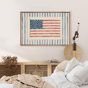 May include: A rectangular wall art piece featuring a watercolor-style American flag centered against a background of vertical blue and white stripes, all enclosed within a light-toned wooden frame that highlights the patriotic design elements.