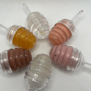 May include: Six clear plastic honey dipper containers with different colored lip glosses inside. The glosses are gold, brown, pink, white with glitter, and two shades of pink.