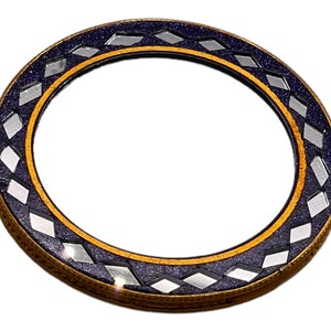 Può includere: Uno specchio rotondo con una cornice decorativa. La cornice è realizzata in un materiale blu scuro con una bordura dorata e un motivo a rombi.