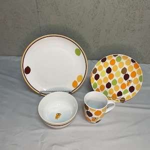 Puede incluir: Un juego de vajilla de cerámica blanca con diseños de hojas y búhos. El juego incluye un plato grande con borde marrón y amarillo, un plato más pequeño con un patrón de hojas, un cuenco y una taza. La paleta de colores incluye blanco, marrón, amarillo y verde.