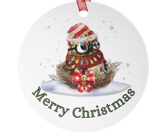 May include: A round white Christmas ornament with a cartoon owl wearing a red and white striped hat, red scarf, and glasses. The owl is surrounded by colorful Christmas lights and is sitting in a nest. The ornament has the text "Merry Christmas" written in green letters.