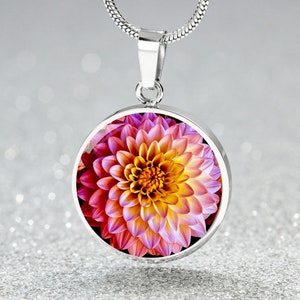 May include: A silver necklace with a round pendant featuring a close-up image of a pink and yellow dahlia flower.