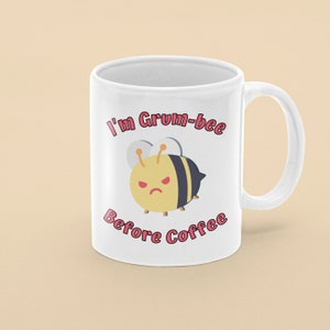 May include: White ceramic coffee mug with a cartoon bee illustration and the text "I'm Grum-bee Before Coffee" in pink.