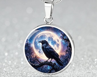 May include: A silver-toned circular pendant necklace featuring a detailed graphic of a black raven perched on a tree branch against a large, glowing full moon in a dark blue night sky. The pendant hangs from a matching silver-toned snake chain.