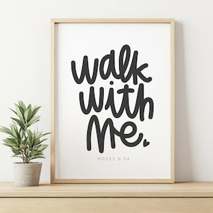 Könnte beinhalten: Ein gerahmter Druck mit dem Text "walk with Me" in schwarzer Schrift. Darunter steht "MOSES 6:34". Der Rahmen ist hellbraun. Links vom Rahmen steht eine kleine Topfpflanze.