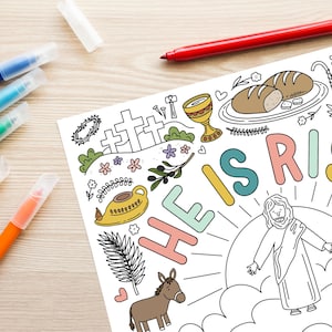 May include: A coloring page with the words "HE IS RISEN" in colorful letters, featuring illustrations of crosses, bread, a chalice, and Jesus. Several colored markers are visible on a light wood surface.