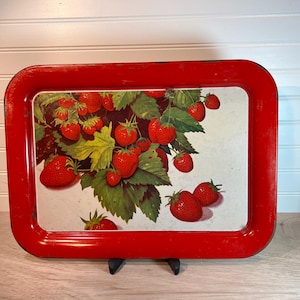 May include: A rectangular red metal tray with a vintage strawberry design. The tray features a vibrant illustration of ripe red strawberries and green leaves against a white background. The tray's edges are a bright red.