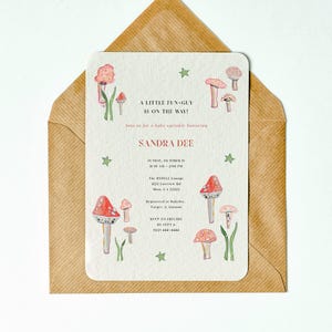Könnte beinhalten: Babyparty-Einladung mit Aquarell-Pilzen in Rot, Rosa und Braun. Die Einladung enthält den Text "A LITTLE FUN-GUY IS ON THE WAY!" und Details für Sandra Dees Babyparty, in einem braunen Umschlag.