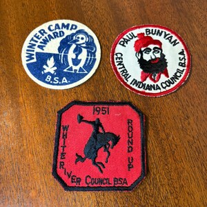 May include: Three vintage BSA patches. One is round with a penguin and the text "Winter Camp Award". Another is round with Paul Bunyan's portrait. The third is red, octagonal, with a cowboy and the text "Round Up".