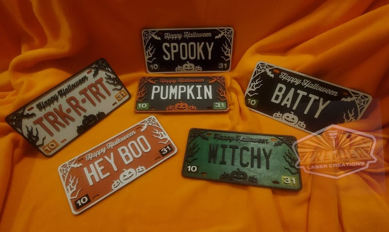 May include: Five wooden Halloween license plate style signs with different spooky phrases. The signs are decorated with bats, pumpkins, and spiderwebs. The phrases are "Spooky", "Pumpkin", "Batty", "Hey Boo", and "Witchy".
