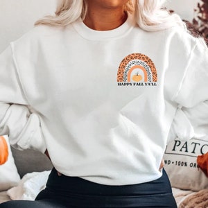 May include: White sweatshirt with a graphic of an orange pumpkin inside a rainbow with a leopard print design. The text "Happy Fall Ya'll" is below the rainbow.