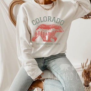 May include: White sweatshirt with a red bear silhouette graphic and the text "COLORADO THE CENTENNIAL STATE EST. 1876".