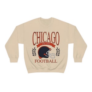 May include: A beige sweatshirt with a vintage-style graphic of a football helmet and the text "CHICAGO EST. 1920 FOOTBALL".
