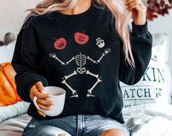 May include: Black sweatshirt with a skeleton juggling a skull and two pumpkins. The pumpkins have happy faces.