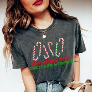 以下が含まれることがあります： キャンディーケーンと「AND NONE FOR GRETCHEN WIENERS」というテキストが書かれたクリスマスをテーマにしたデザインのダークグレーのTシャツです。