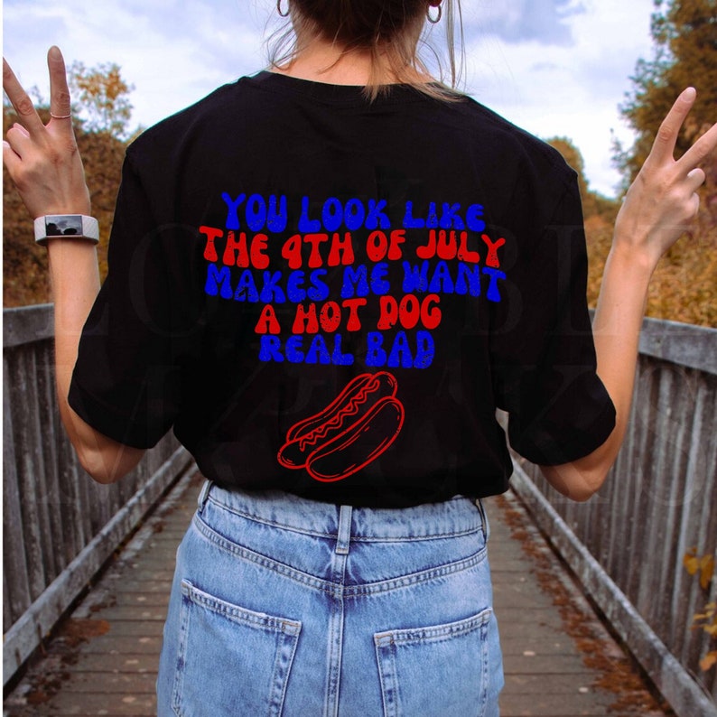 May include: A black t-shirt with the text "You look like the 4th of July makes me want a hot dog real bad" in red and blue lettering. A red and white hot dog is pictured below the text.