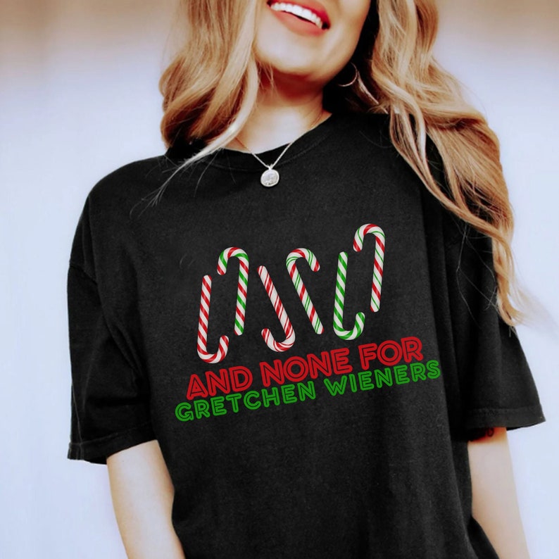 以下が含まれることがあります： 赤と緑のキャンディーケーンのグラフィックと「AND NONE FOR GRETCHEN WIENERS」というテキストが書かれた黒いTシャツ。