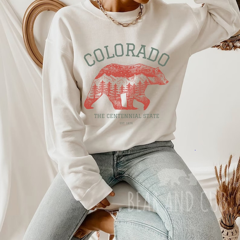 May include: White sweatshirt with a red bear silhouette graphic and the text "COLORADO THE CENTENNIAL STATE EST. 1876".