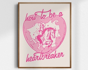 May include: Pink and cream-colored art print in a wooden frame. The print features a pink heart shape with a cowgirl riding a horse, and the words "how to be a heartbreaker" in pink script.