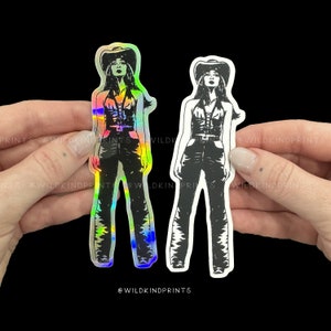 May include: Two stickers of a woman wearing a cowboy hat and a vest. The sticker on the left is iridescent and the sticker on the right is black and white.