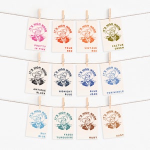 May include: Ten different colour variations of a vintage "It's High Noon" graphic featuring a cowboy with a gun. The colours include: Pretty in Pink, True Red, Vintage Red, Cactus Green, Antique Black, Midnight Blue, Blue Jean, Periwinkle, Sky Blue, Faded Turquoise, Rust, and Dust.