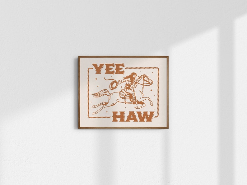 May include: A brown framed print with a white background and a line drawing of a woman riding a horse. The text "Yee Haw" is written in brown letters above and below the image.