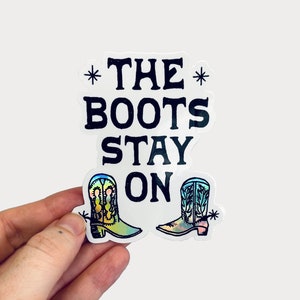 May include: A white sticker with black text that reads "*THE BOOTS STAY ON*" with two colorful cowboy boots on either side of the text.