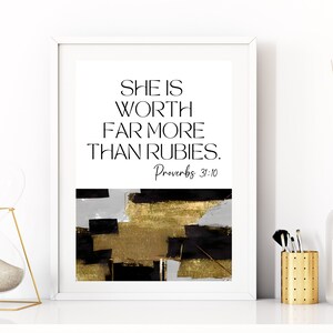 May include: A white framed print with a black and gold abstract design. The print features the text "She is worth far more than rubies. Proverbs 31:10"