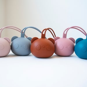 May include: Five silicone baby teethers shaped like bears in different colors: pink, blue, brown, pink, and blue. Each teether has a loop handle.