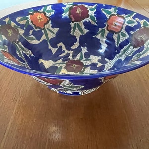 May include: A large blue ceramic bowl with a floral pattern. The bowl has a white background with green leaves and red, orange, and brown flowers.