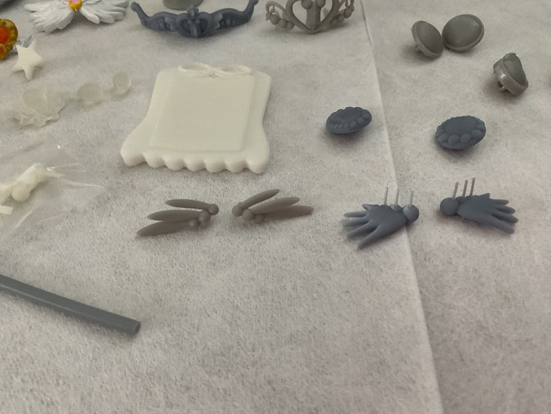 May include: Assortment of grey plastic dollhouse furniture and accessories, including a small picture frame, a pair of wings, a pair of hands, and a pair of round decorations.