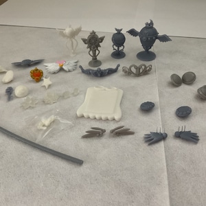 May include: A collection of white and grey 3D printed accessories, including crowns, wands, and other decorative pieces.