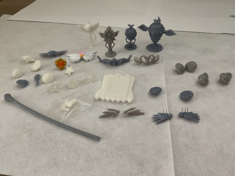 May include: A collection of white and grey 3D printed accessories, including crowns, wands, and other decorative pieces.