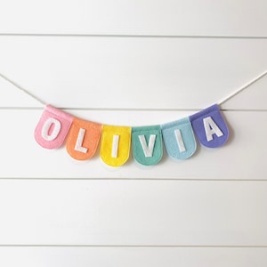 Olivia felt name banner on pastel rainbow scallop shaped flags. hanging banner on nursery shiplap wall