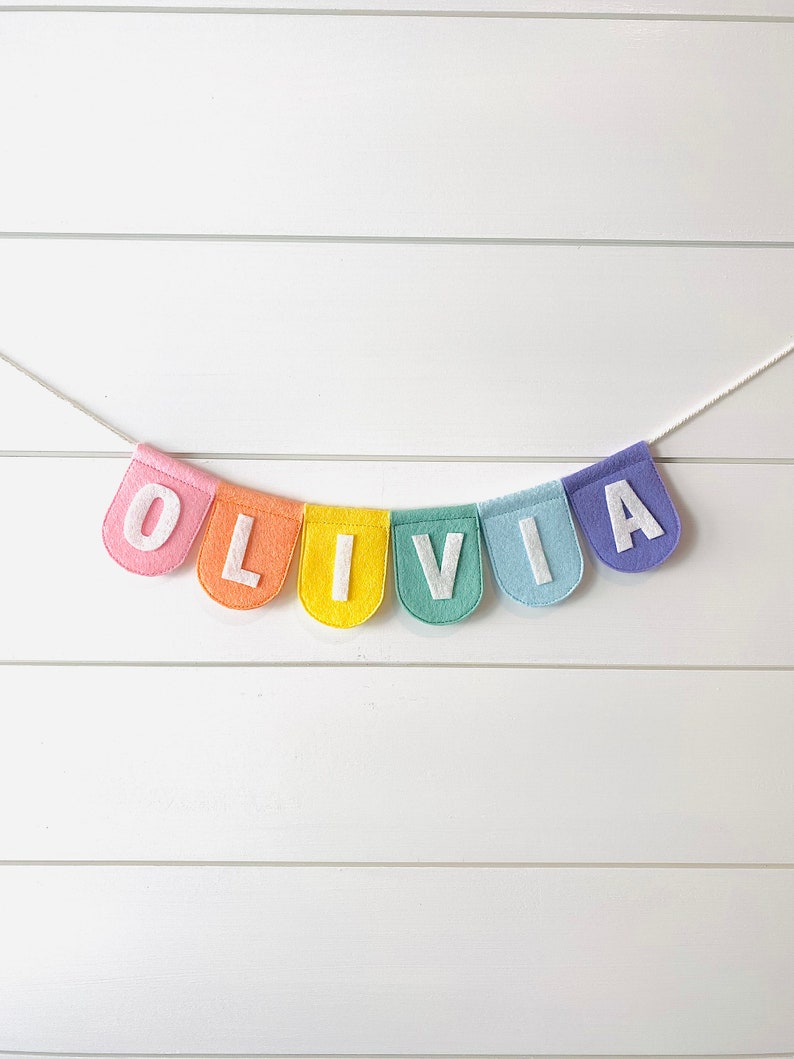 Olivia felt name banner on pastel rainbow scallop shaped flags. hanging banner on nursery shiplap wall