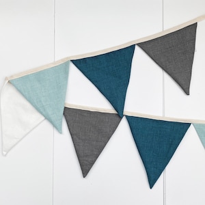 May include: A bunting banner with alternating blue, gray, and white triangular flags. The flags are made of a textured fabric and are connected by a white ribbon.