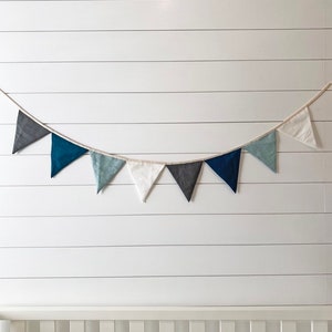 Linen bunting banner with grey, navy, blue and white flags hanging on top of nursery crib