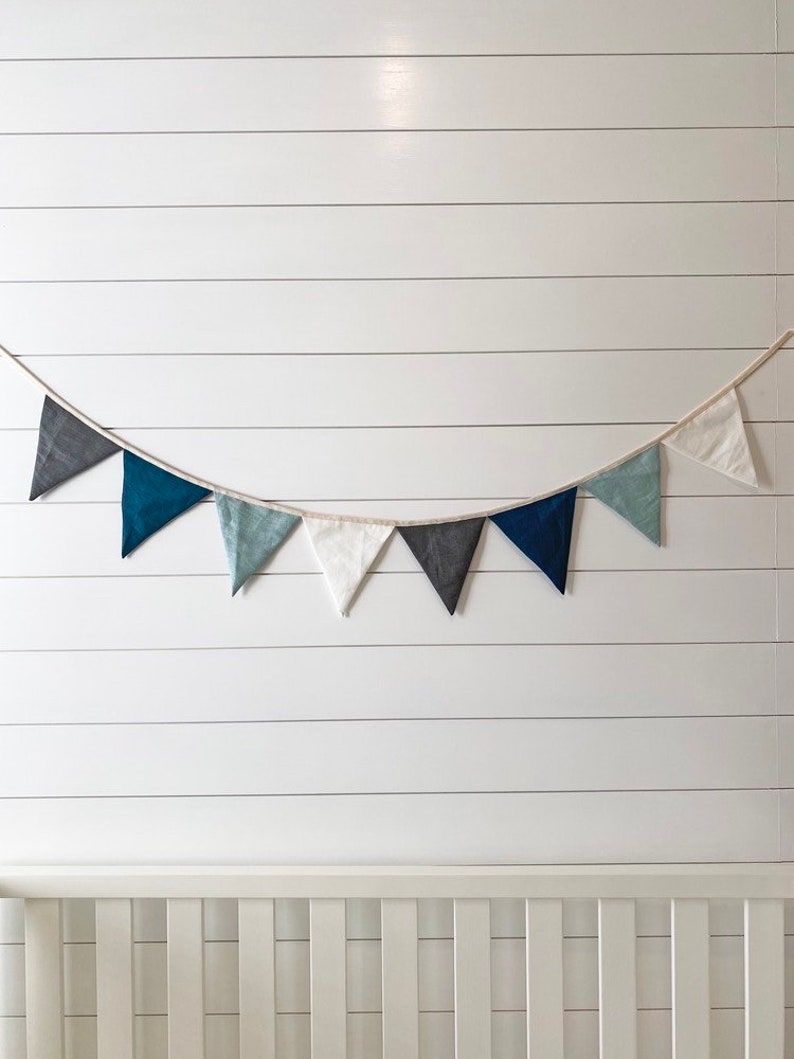 Linen bunting banner with grey, navy, blue and white flags hanging on top of nursery crib